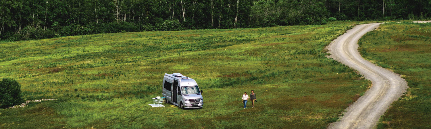 A Mercedes Benz RV parked in the middle of a camping ground, while two people walk away.